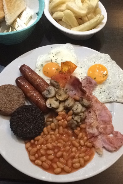 Black pudding, ham, sausages, mushrooms, beans in tomato sauce and fried eggs; french fries with toast and butter in the back